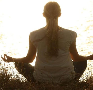 A woman sitting in a field with her hands on her knees in meditation.