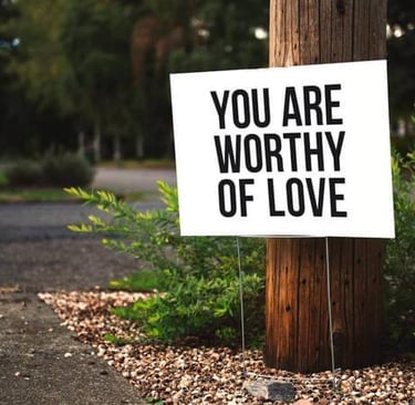 “You are worthy of love” sign posted along a quiet outdoor path.