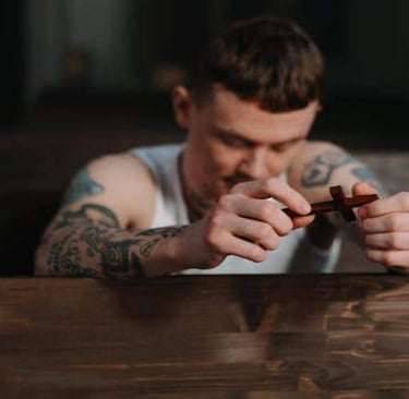 A man with tattoos on his arm, kneeling and holding a small cross