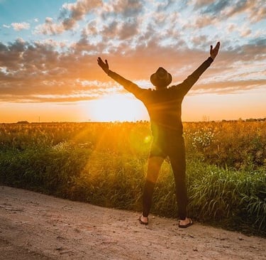 a man standing on a dirt road with his arms up in the air