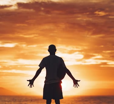 A person stands with open arms at sunset, expressing wonder, surrender, and spiritual searching.