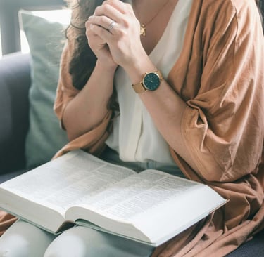 a woman sitting with a bible on her knee and praying