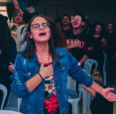 Young person singing with hand on chest and arm extended, surrounded by others in worship.