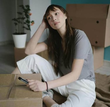 a woman sitting on a cardboard box with a cell phone, wondering