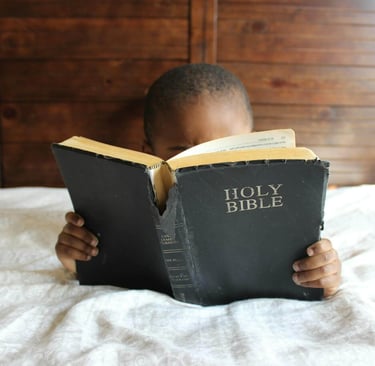 a young boy is reading a book while holding a bible