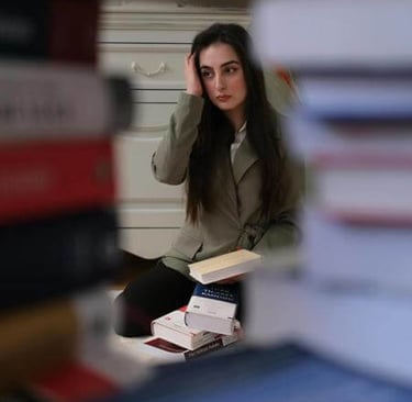 Individual reading a book, viewed through a tunnel of stacked books in a cozy indoor setting.