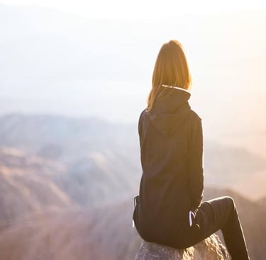 A person sitting on top of grey rock overlooking mountain during daytime