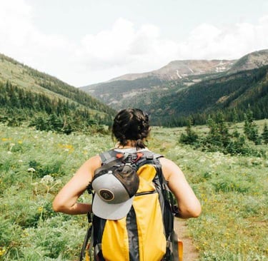 Person hiking through a green mountain valley with a backpack.