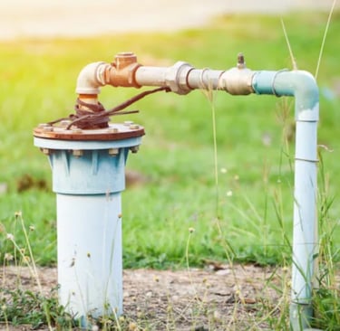 Outdoor water well pump head and pvc pipe plumbing installation in a green grass field.
