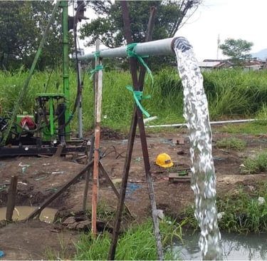 A portable water well drilling rig pumping a steady stream of clear water from a pipe into a muddy field.