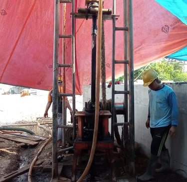 Construction workers operating a vertical borehole drilling rig for groundwater well installation.
