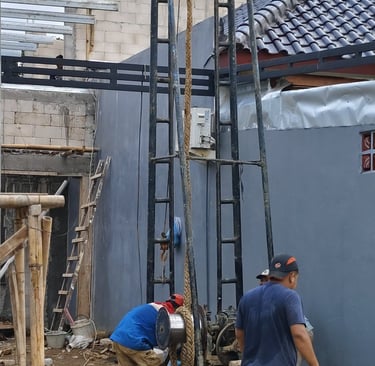 Construction workers operating a vertical deep well drilling machine for water access at a residential site.