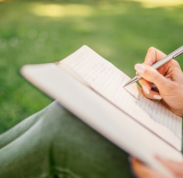 a woman person holding a pen and writing on a notebook outside