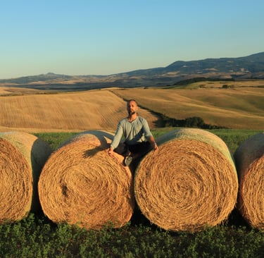 Life coach Abhisek sitting on a hay bale in the sunshine, wuth rolling hills behind him. happiness