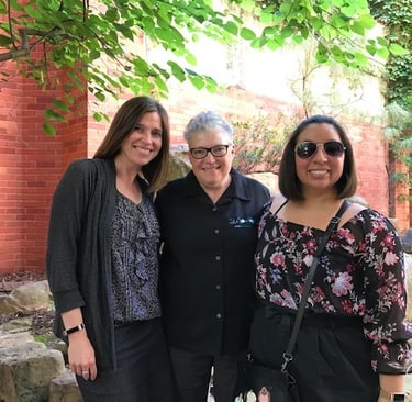 three women standing next to each other in front of a brick building