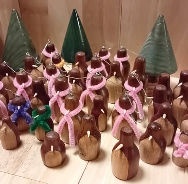 A group of turned wooden penguins in dark wood with light front and light beak. Some wearing pipecleaner scarfs
