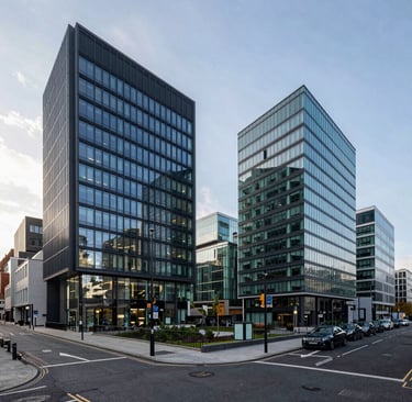 A wide-angle professional photograph of a modern commercial district in the United Kingdom, featuring sleek glass buildings, clean streets, and a professional atmosphere during a bright, sunny morning. The color palette features deep navy blue reflections and clean teal glass accents. High-quality corporate realism, highly detailed, soft natural lighting.
