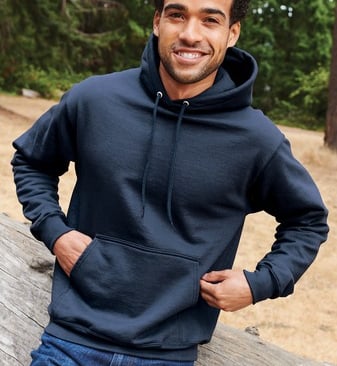 a man in a blue hoodie and jeans standing in front of a log cabin