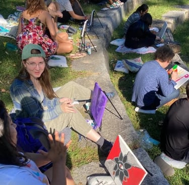 A group of students painting on canvases at an outdoor art workshop in a park.