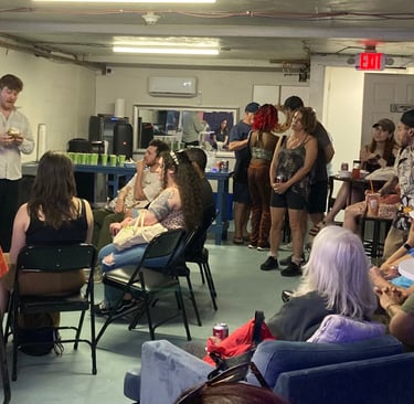 A group of people sitting and standing in a basement community room attending an educational presentation.