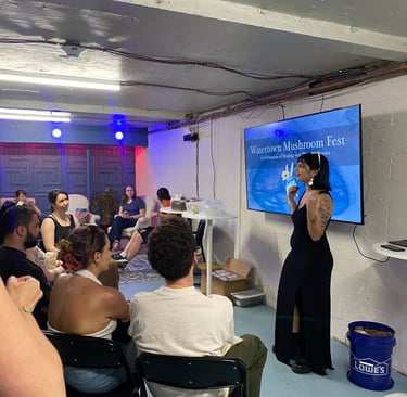 A speaker presents at Watertown Mushroom Fest to an engaged audience in a modern studio space.