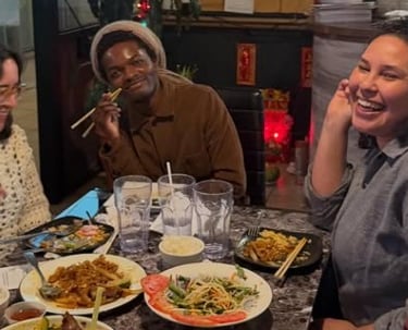 Diverse friends laughing and eating Thai food at a restaurant with noodles and rice dishes.