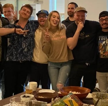 A diverse group of smiling friends posing together behind a table of party snacks and appetizers.