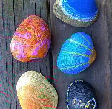Hand-painted decorative seashells with colorful patterns and beads on a rustic wooden surface.