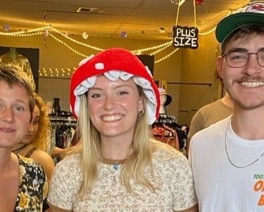 Three smiling friends posing at a vintage clothing store or thrift shop.