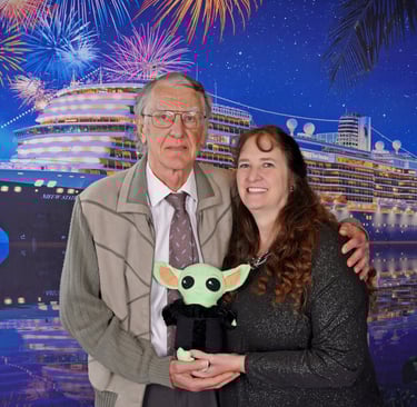 A couple standing in front of a cruise ship backdrop holding a little green companion