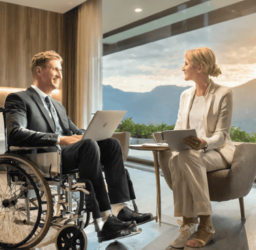 Rollstuhlfahrer sitzt einer Dame bei einem Beratungsgespräch in einem Hotelzimmer gegenüber