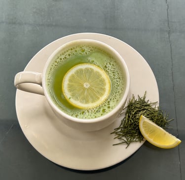A cup of frothy green matcha tea with a lemon slice garnish and loose tea leaves.