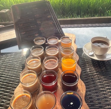 A colorful coffee and tea tasting flight on a wooden tray with a lush green rice field background in Bali.