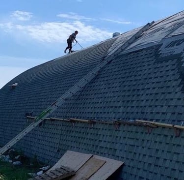 Professional roofers installing IKO shingles on a large curved barn roof using safety harnesses.
