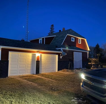 Red residential barn-style house with a two-car garage illuminated at night with a truck parked in the driveway.
