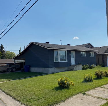 A modern charcoal grey bungalow house with a green lawn and blue sky on a suburban street.