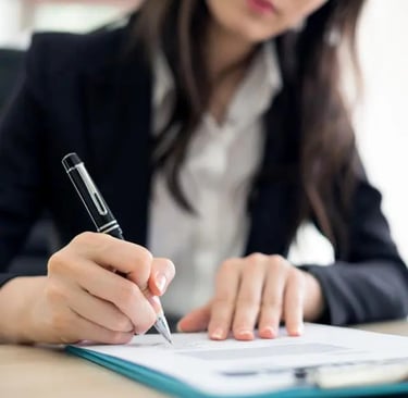 A person in business attire is writing on a business selling using a pen. The image focuses on their hands and the document.