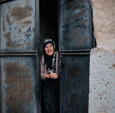 Elderly woman in a headscarf peeking through a weathered metal door in Cappadocia, Turkey