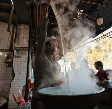 ea vendor pouring hot chai from height at a street stall in Old Delhi.