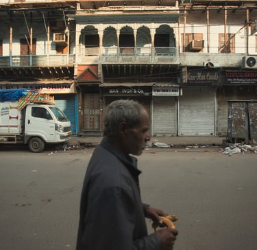 Man walking past closed shops and old façades on a quiet Old Delhi street.