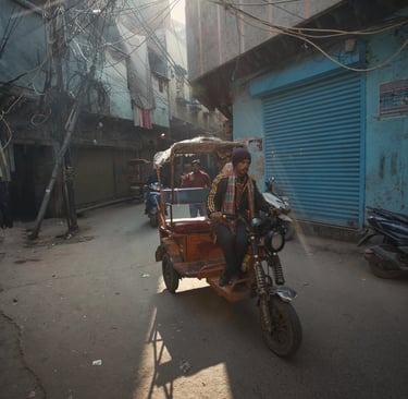 Motorized rickshaw driving through a narrow Old Delhi street in morning light.