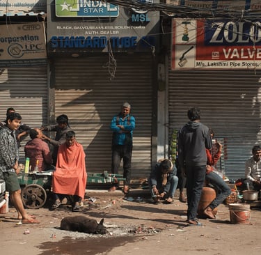 Street barber and locals gathered outside shuttered shops in Old Delhi