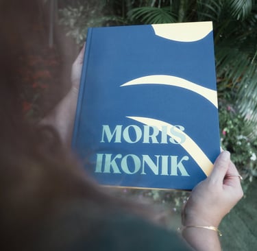 Person holding Moris Ikonik book against tropical background in Mauritius