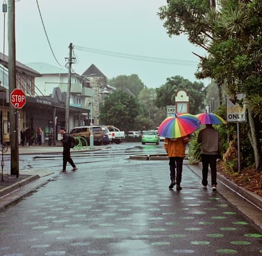 Colourful rainbow umbrellas in use while the owners walk along a street on a dreary day.
