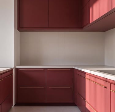 Matte ruby red kitchen cabinets with gold handles and quartz countertops in a minimalist kitchen.