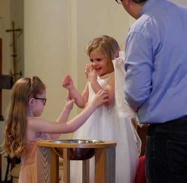2 young children looking happy at a church font as a Vicar baptises them. 