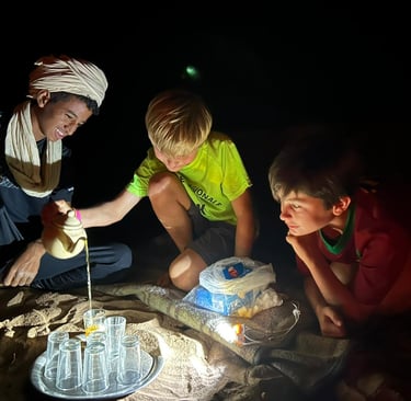 Two boys in the desert being shown how to pour tea Moroccan style
