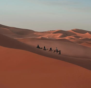A camel train crosses the ridge of a desert dune field