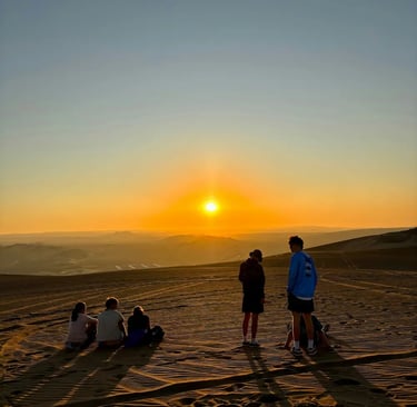 A group of people with backs to camera in the desert watching the sunset