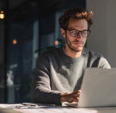 A focused professional man with glasses working on a laptop in a modern office.